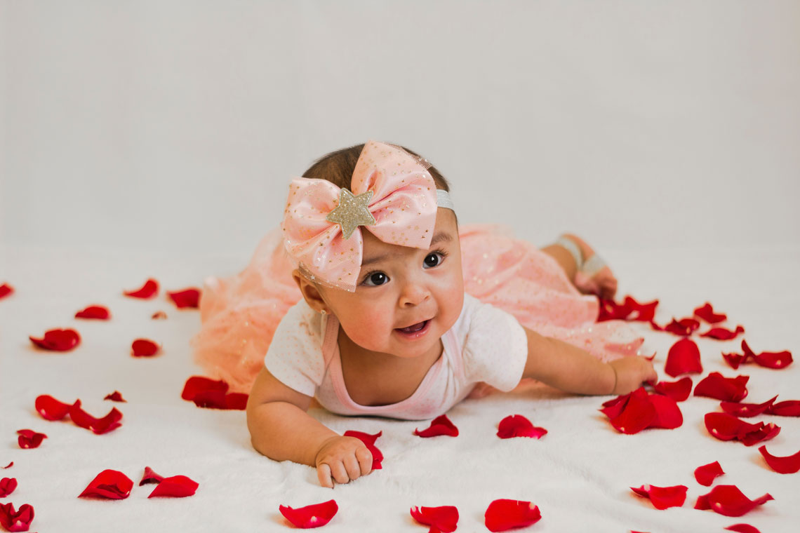 Toddler in a pink dress surrounded with rose petals